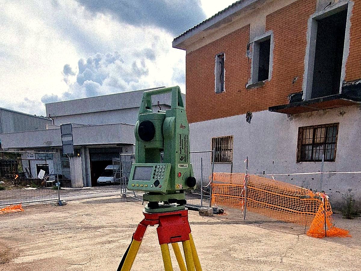 Stazione totale su treppiede davanti a un fabbricato in cantiere